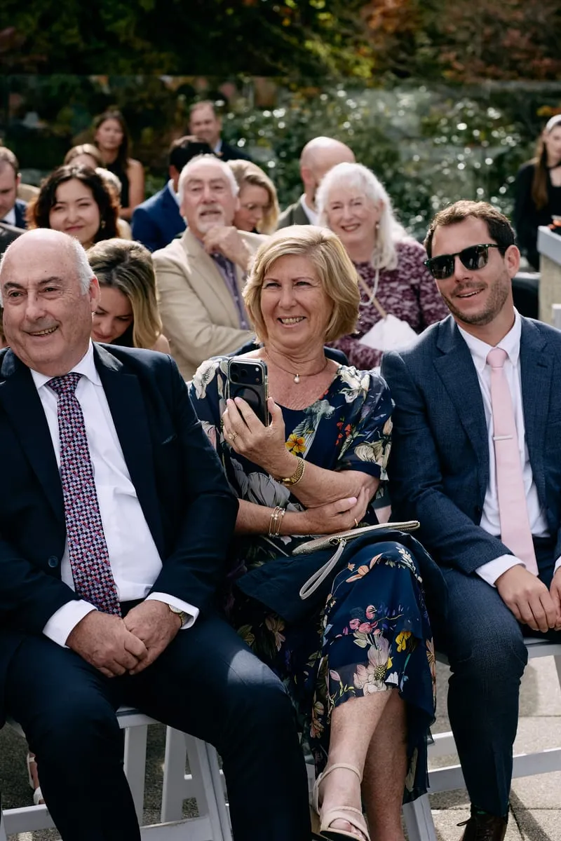 Guests in the second row laugh, one of them filming on her phone.