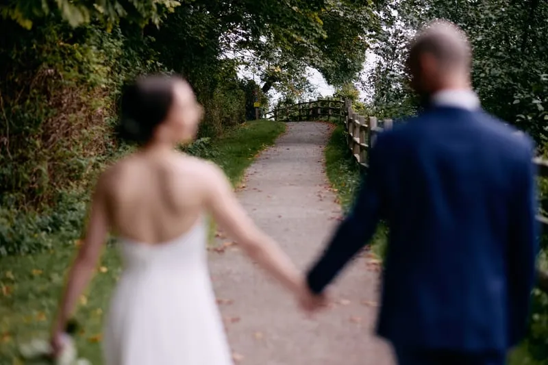 Olivia and James walk away up the path holding hands, both softly out of focus.