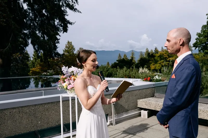 Olivia reads her vows into a microphone as James listens, the mountains behind them.