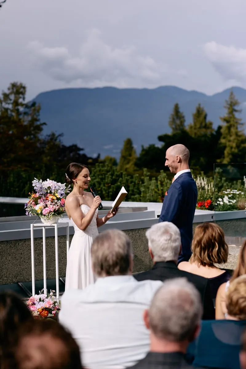 Seen past the guests' heads, Olivia reads to James under a grey sky with the mountains beyond.