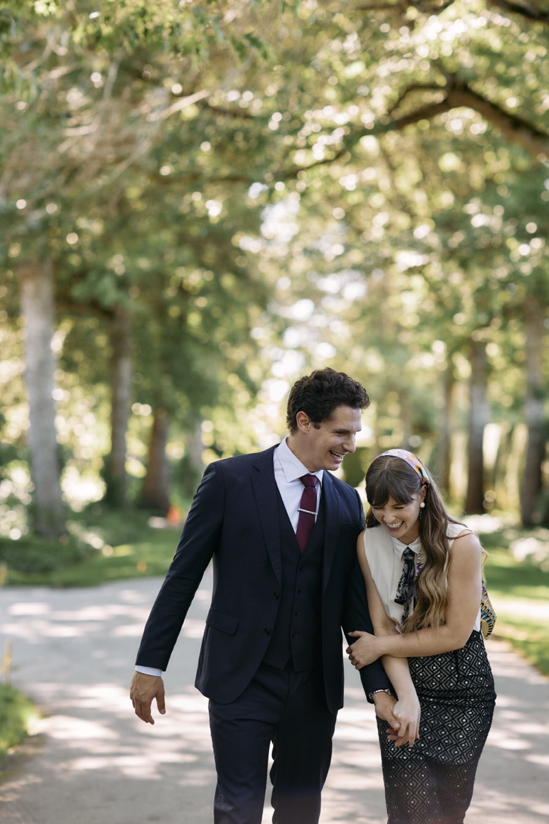 Bride and groom walking a tree-lined avenue in formal gardens.