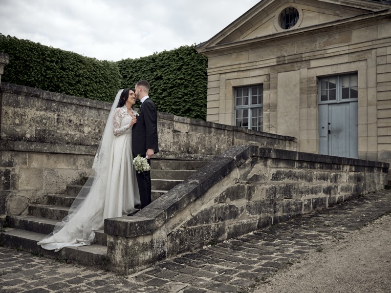 Black and white portrait of a bride and groom among tall hedges.