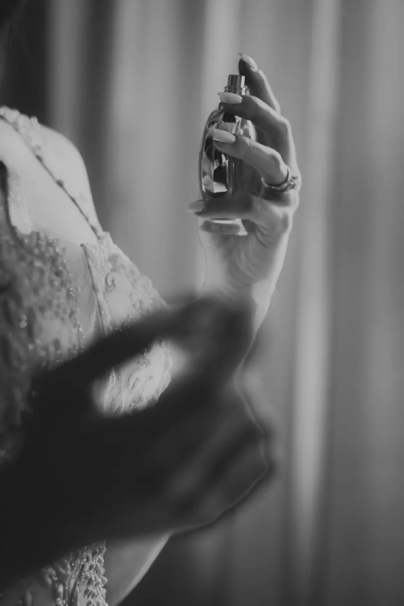 Black and white photograph of a bride's hand holding a bottle of perfume, her ring catching the light.