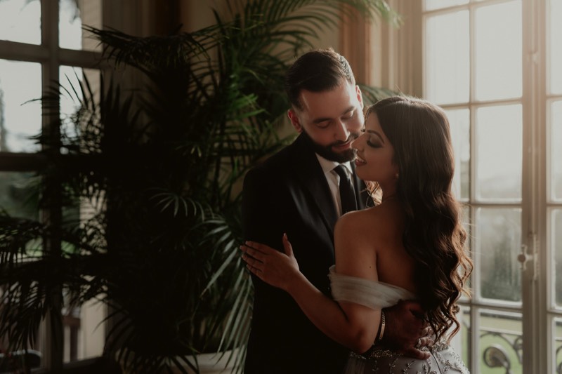 Black and white portrait of a bride and groom among tall hedges.
