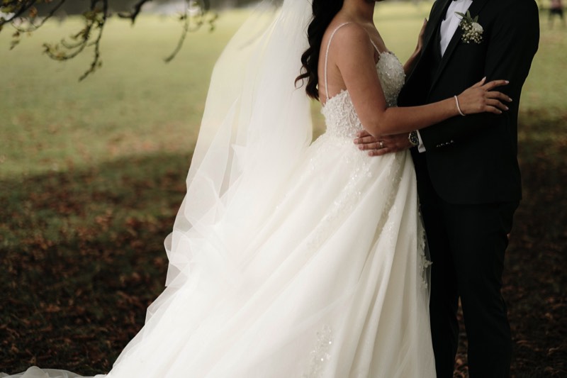 Bride in a lace gown holding her bouquet on a garden path.