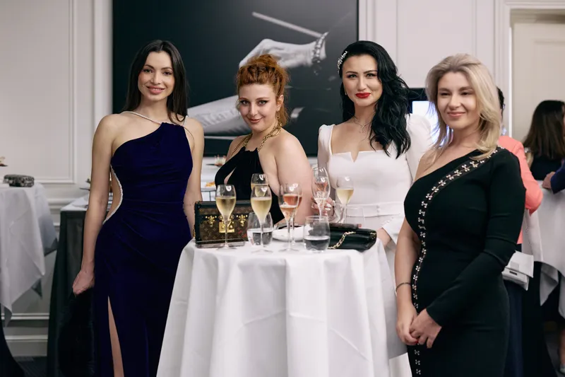 Four guests in evening dresses pose with champagne glasses at a cocktail table.
