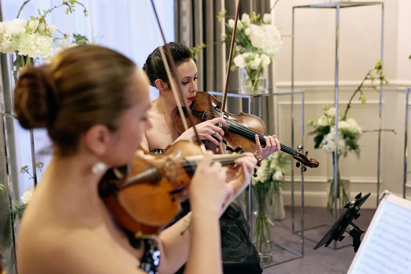 A violinist in a black dress plays beside white flowers at a wedding reception.